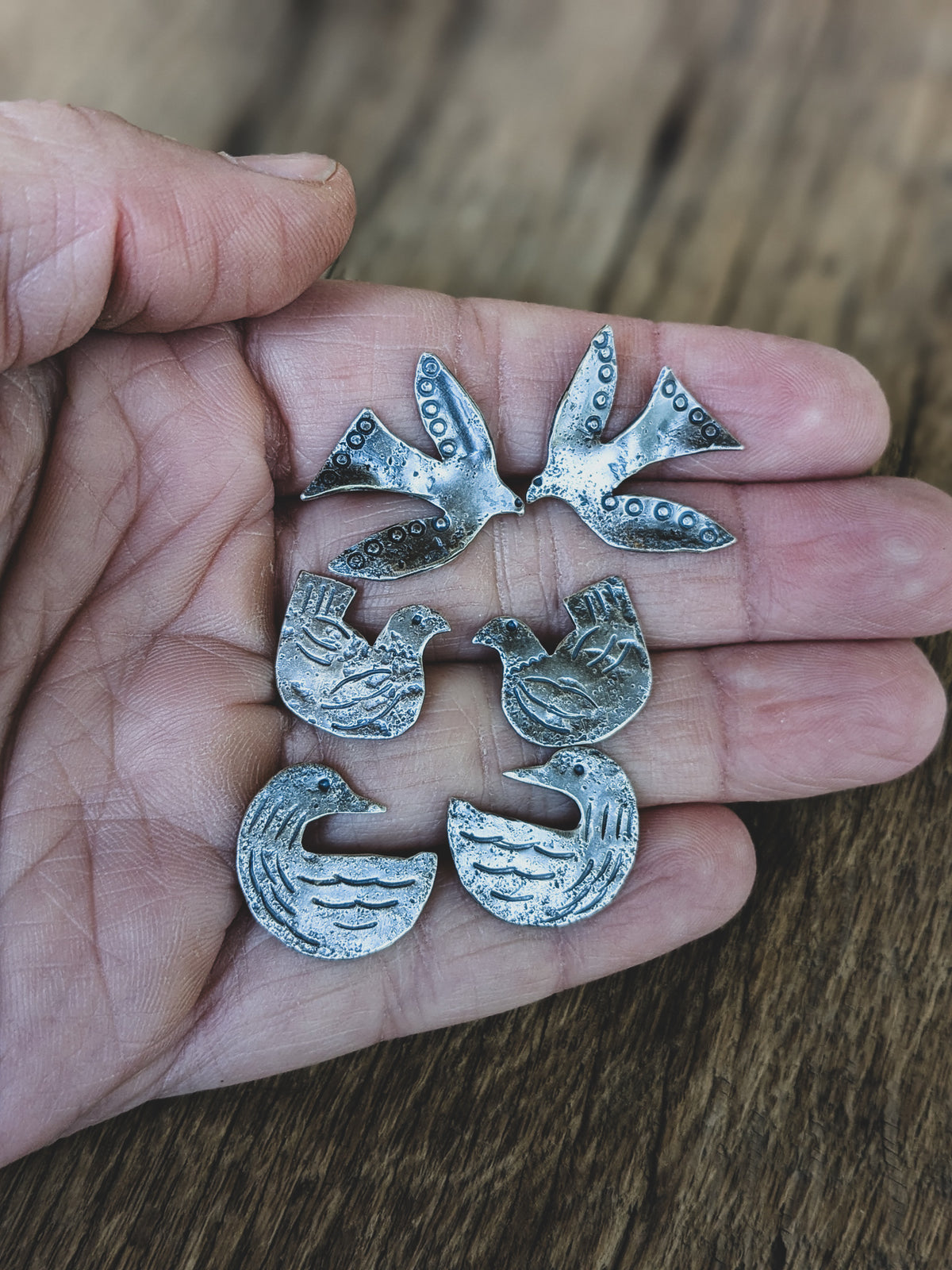 Hand holds three sterling silver earring pairs featuring flying birds, loons and chickens stamped in a folk art style
